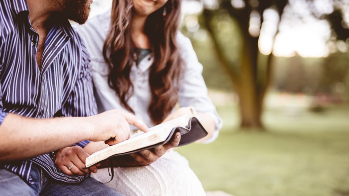 Zwei Personen sitzen draußen auf einer Bank und lesen gemeinsam Bücher in einem Park.