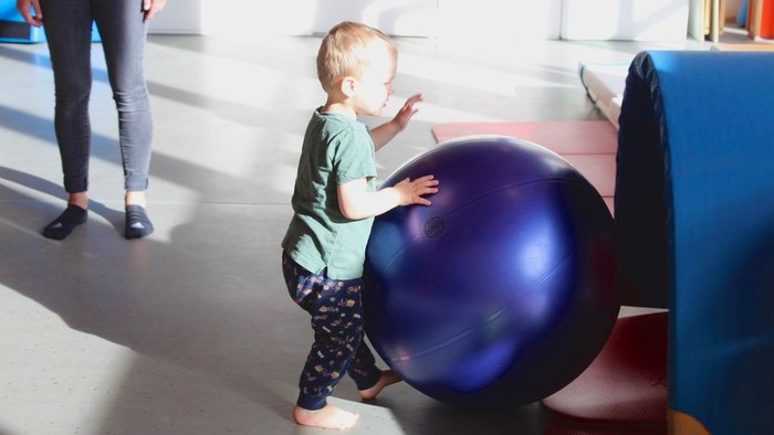 Ein kleines Kind spielt mit einem großen Gymnastikball in einem Spielbereich.