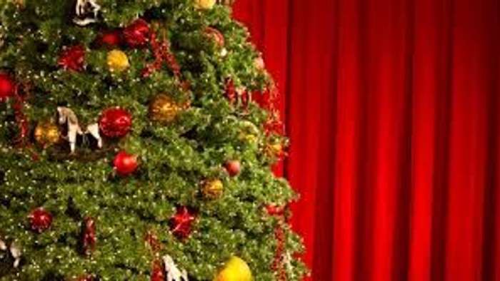 En juletree med røde og gule pynt med røde gardiner i baggrunden