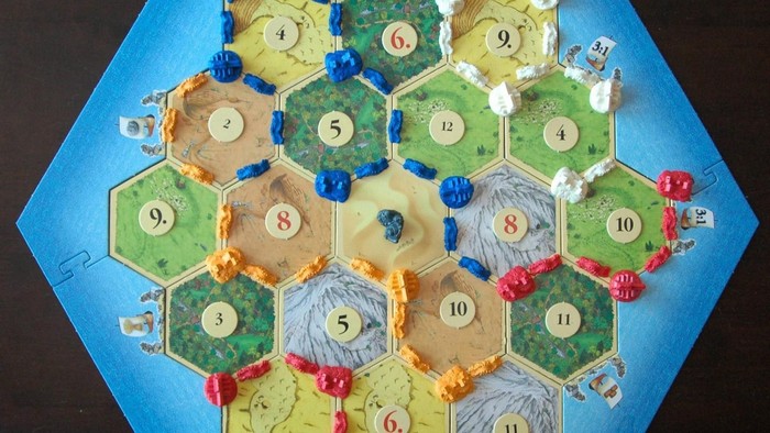Ein Brettspielaufbau mit einer hexagonalen Karte mit nummerierten Plättchen, Arbeitern und Ressourcenmarkern.