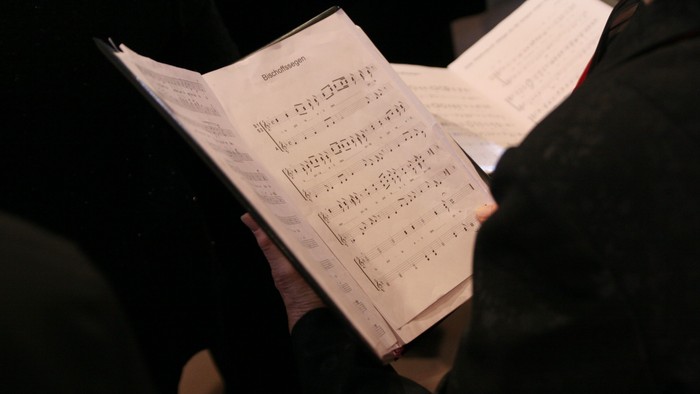 Eine ältere Dame hält ein aufgeschlagenes Liedblatt in der Hand. 