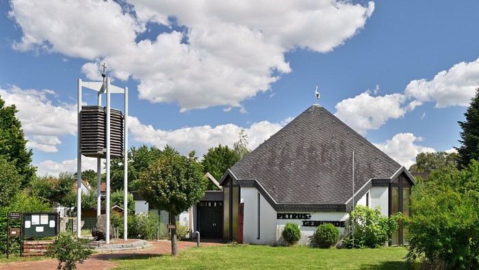 Moderne Kirche mit steilem Dach und hohem Glockenturm in einer üppigen, grünen Außenanlage.