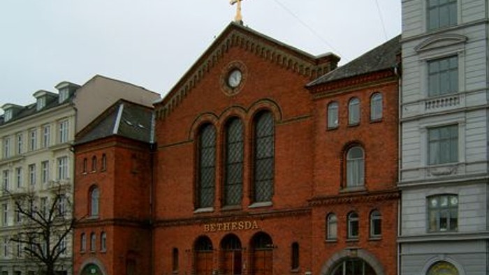 Røde kirke med tårn og klokke, placeret mellem andre bygninger.