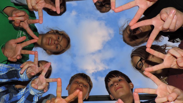 Eine fröhliche Gruppe macht Friedenszeichen und lächelt in einen klaren blauen Himmel hinauf.