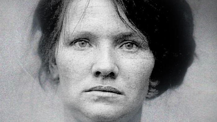 Sort-hvid mugshot af en kvinde med kort, glat hår, der kigger direkte frem med et neutralt udtryk.