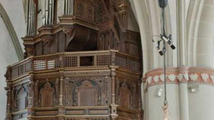 Komplexe hölzerne Kirchenorgel mit verzierten Pfeifen und dekorativem Kronleuchter in historischem architektonischem Ambiente.