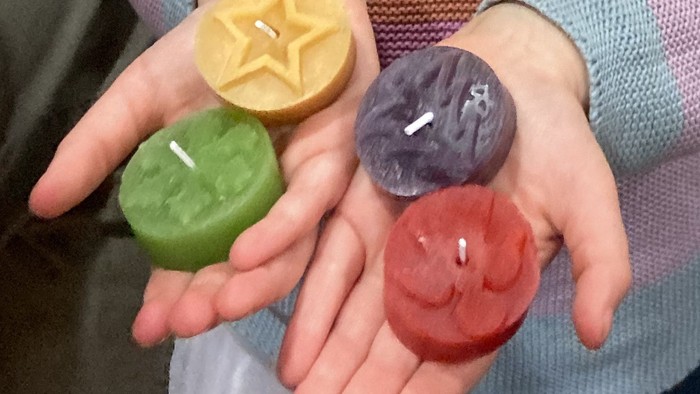 Bunte sternförmige Kerzen in Form von Früchten, die in Händen gehalten werden.