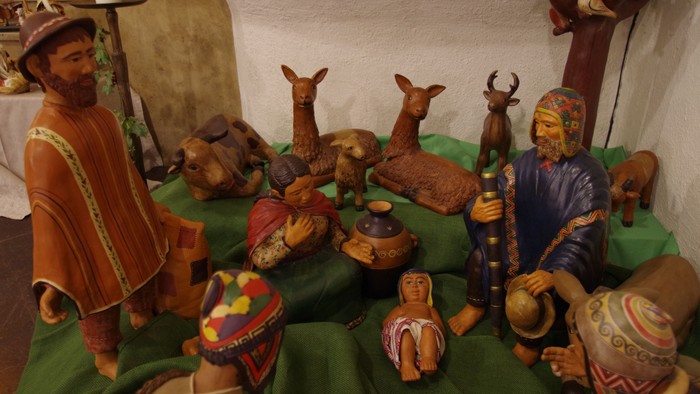 Die Szene zeigt verschiedene Holzfiguren, darunter Menschen und Tiere, die auf einem grünen Tuch angeordnet sind.