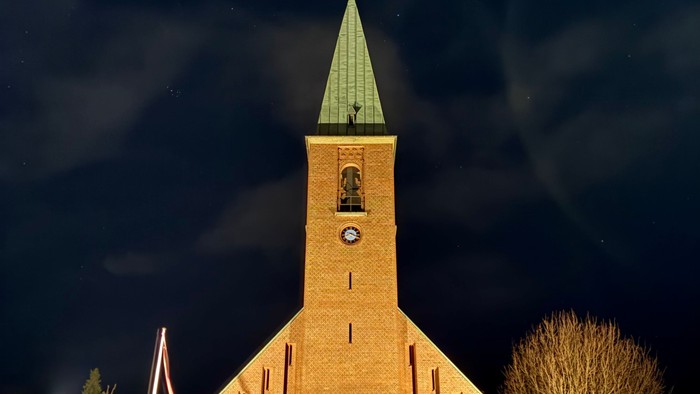 En smukt oplyst kirke med et klokketårn og slørede billygter mod en nattehimmel.