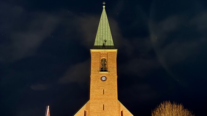 En smukt oplyst kirke med et klokketårn og slørede billygter mod en nattehimmel.