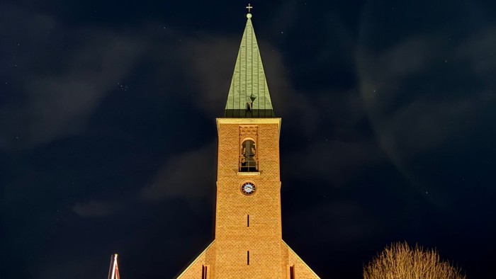En smukt oplyst kirke med et klokketårn og slørede billygter mod en nattehimmel.