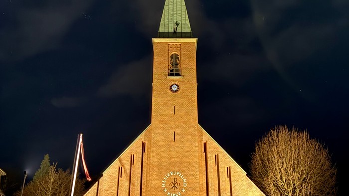 En smukt oplyst kirke med et klokketårn og slørede billygter mod en nattehimmel.