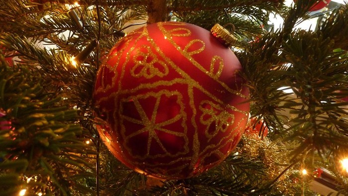 Roter Weihnachtschmuck mit goldener Verzierung hängt am Baum.