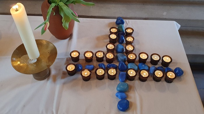 Kerzen, die kreuzförmig auf einem Tisch mit einer Topfpflanze arrangiert sind.