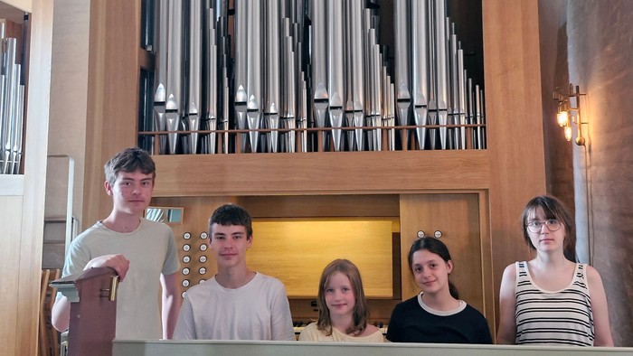 Fire personer poser foran et stort pibeorgel i en kirke eller et kapel.