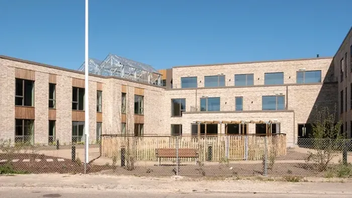 Moderne murstensbygningskompleks med udendørs opholdsområde og indhegnet område under klar himmel.