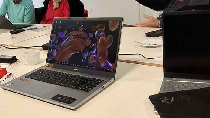 Eine Gruppe von Personen in einem Klassenzimmer mit Laptops und einem Vortragenden vorne.