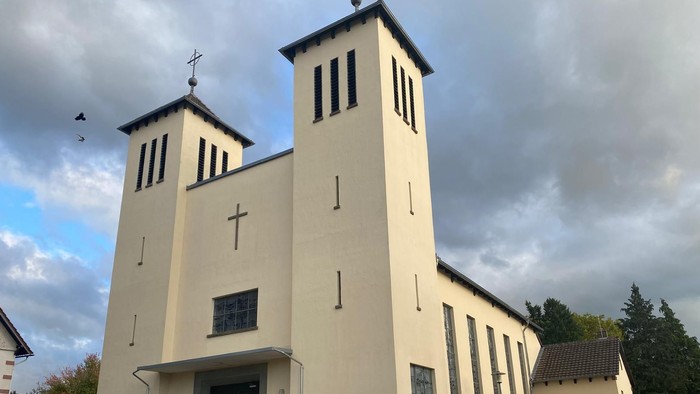 Moderne Kirche mit Zwillingstürmen, hellem Äußeren und gestaltetem Eingangsbereich unter bewölktem Himmel.