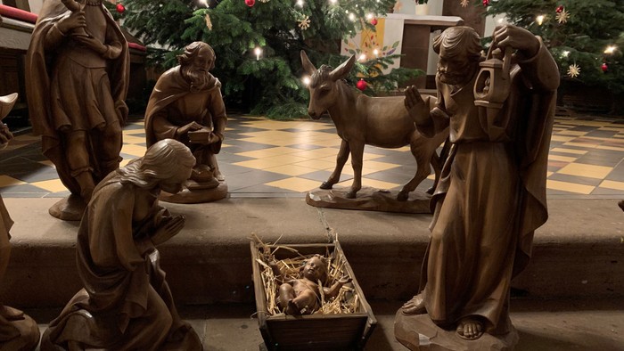 Bronze-Krippe mit Darstellung der Geburt Jesu, inklusive Figuren, Tieren und einer Krippe unter einem geschmückten Weihnachtsbaum.
