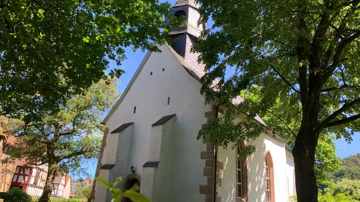 Eine malerische weiße Kirche mit Glockenturm, eingebettet zwischen üppigen grünen Bäumen.