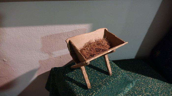 Eine Holzkrippe mit Stroh steht vor einer Wand.