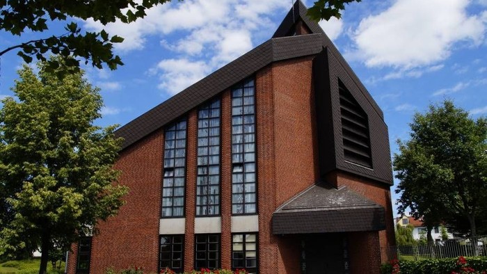 Das Bild zeigt eine moderne Ziegelkirche mit großen Fenstern und einem spitzen Dach.