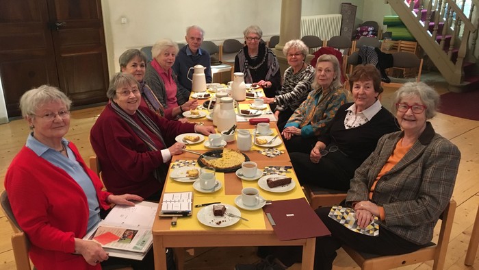Ein Gruppe älterer Frauen sitzt an einem Tisch mit Tee und Gebäck