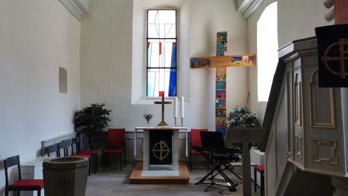Kirchlicher Innenraum mit Altarraum, Buntglasfenster und Holzbänken