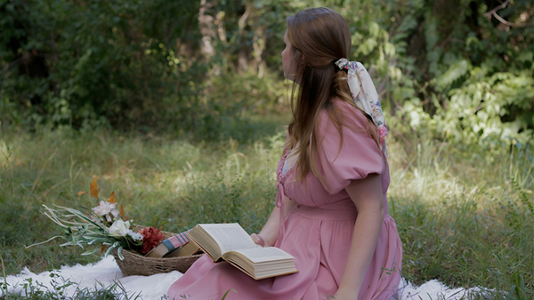 Frau im Kleid mit Buch in der Hand sitzt auf Wiese