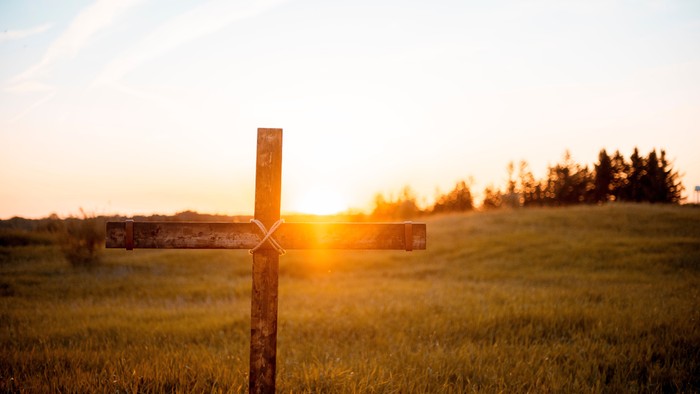 Ein rustikales Holzkreuzschild steht auf einer grasbewachsenen Wiese während eines goldenen Sonnenuntergangs.