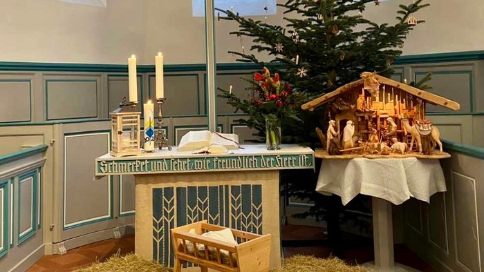 In der Kirche steht ein geschmückter Weihnachtsbaum neben einem Krippenspiel.