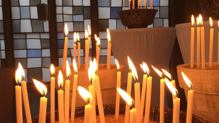 Kerzen in einer Kirche mit bunten Glasfenstern entzündet.