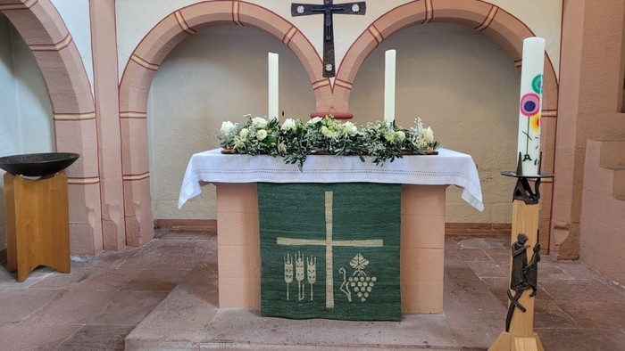 Verzierter Altar mit floralem Mittelstück, Wein- und Traubensymbolen sowie aufrecht stehenden Kerzen in einer Kirchenumgebung.