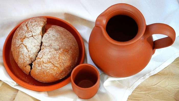Ein Laib Brot in einer Schüssel neben einer Karaffe mit Flüssigkeit und einer kleinen Tasse.