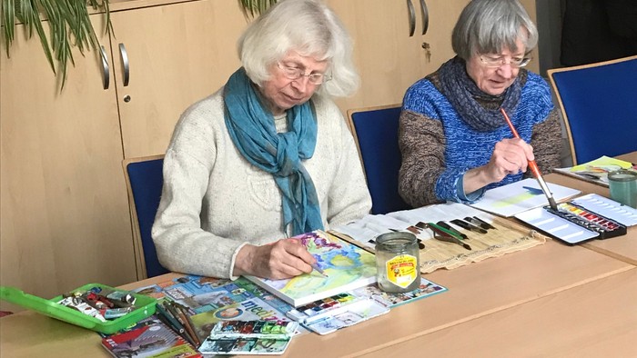 Zwei ältere Frauen sitzen an einem Tisch und schauen in ein Buch.