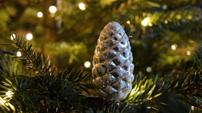 En glitrende pyknøde hænger i et juletræ med lys.
