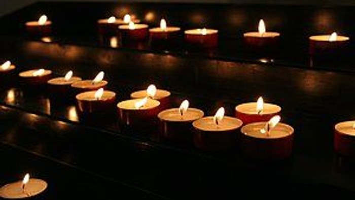 Reihen von brennenden Kerzen, ordentlich auf einer dunklen Oberfläche angeordnet, die warmes, flackerndes Licht werfen.