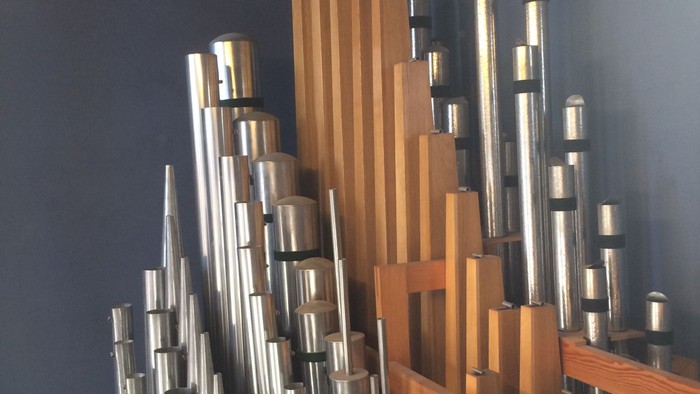 Eine Nahaufnahme einer Orgel mit Holzrahmen und zahlreichen metallischen Pfeifen in unterschiedlichen Längen und Größen.