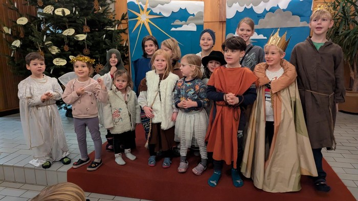 Kinder in Kostümen stehen vor Weihnachtsdekoration