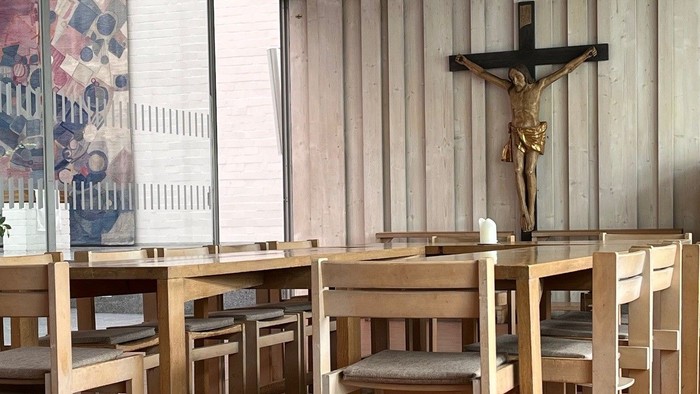 Ein ruhiger Kapelleninnenraum mit hölzernen Kirchenbänken, einem Kruzifix und großen Fenstern, die natürliches Licht hereinlassen.