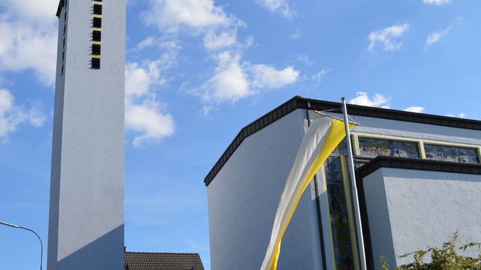 Moderne Kirche mit hohem Glockenturm und geschwungenem Eingangsüberdach unter einem strahlend blauen Himmel.