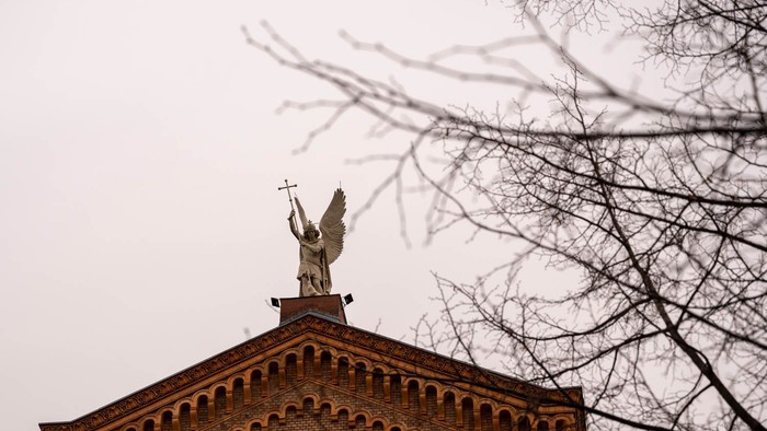 Ein Engel mit Kreuz auf einem Ziegelgebäude, umgeben von kahlen Bäumen