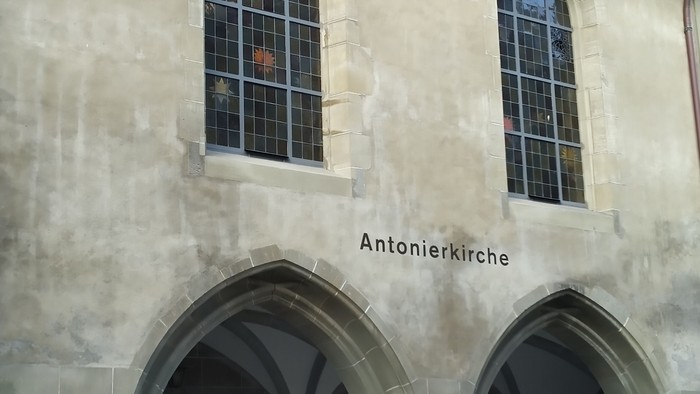 Historische Kirchenfassade namens Antonierkirche mit bogenförmigen Eingängen und farbigen Glasfenstern darüber.