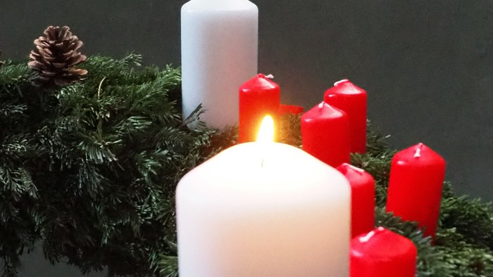 Weiße und rote Kerzen auf Kieferzweigen mit einer roten Schleife.