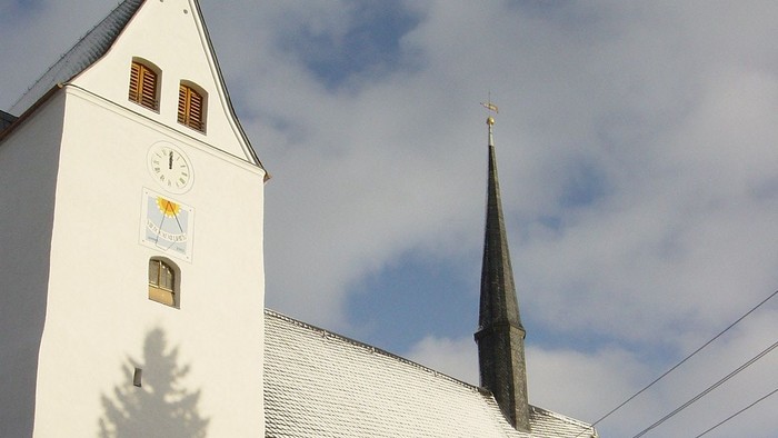 Weiße Kirche mit hohem Turm und schneebedeckten Büschen davor