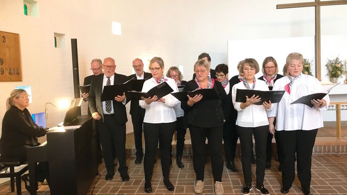 Et kor synger sammen i en kirke med en pianist, der akkompagnerer dem.