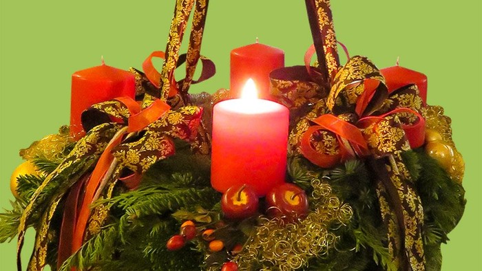 Ein festlicher Kranz mit Kerzen und Dekorationen vor grünem Hintergrund
