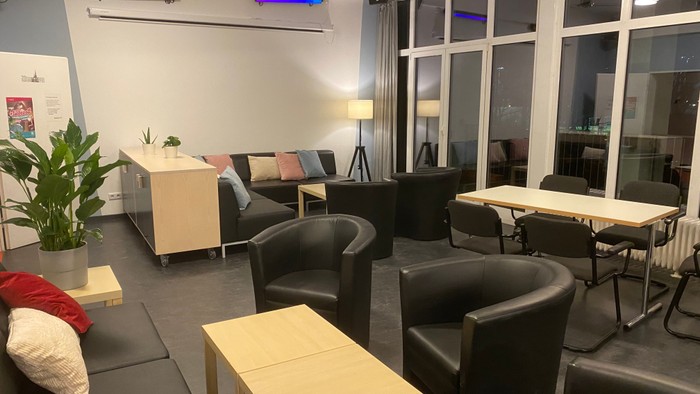 Moderner Loungebereich mit gemütlichen Sitzgelegenheiten, Tischen und großen Fenstern sowie farbenfrohen Deckenleuchten.