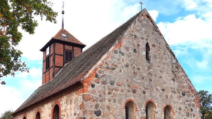 Steinige Kirche mit Turm auf grünem Hügel unter blauem Himmel
