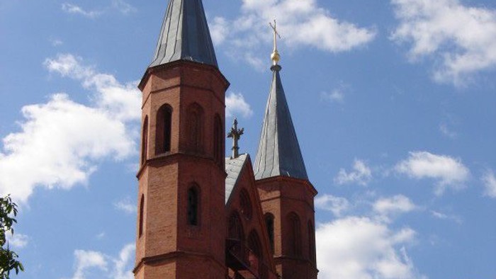 Zwei Kirchtürme mit Kreuz und Wetterfahne vor blauem Himmel